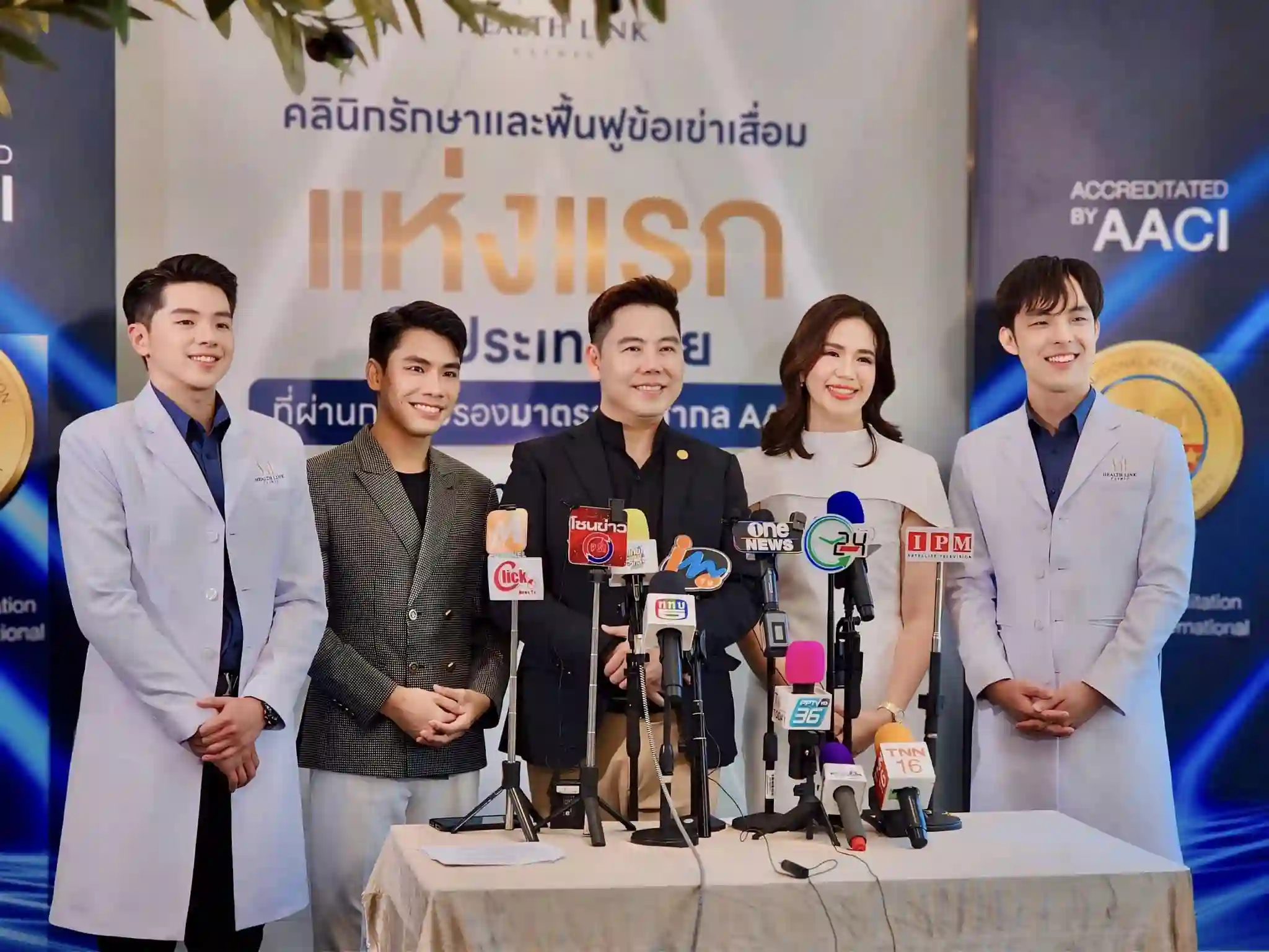 ภาพการแถลงข่าวของคลินิกรักษาและฟื้นฟูข้อเข่าเสื่อมแห่งแรกในประเทศไทยที่ได้รับการรับรองมาตรฐาน AACI ในภาพมีทีมแพทย์และผู้บริหารของคลินิกยืนเรียงกันอยู่หลังไมโครโฟนและโลโก้สื่อมวลชนหลายช่อง ทั้งหมดแต่งกายด้วยชุดทางการและมีรอยยิ้ม พื้นหลังเป็นแบนเนอร์ที่มีข้อความเน้นถึงการเป็นคลินิกแห่งแรกที่ได้รับการรับรองมาตรฐานระดับสากล ภาพนี้เน้นถึงความน่าเชื่อถือและความเป็นมืออาชีพของคลินิก